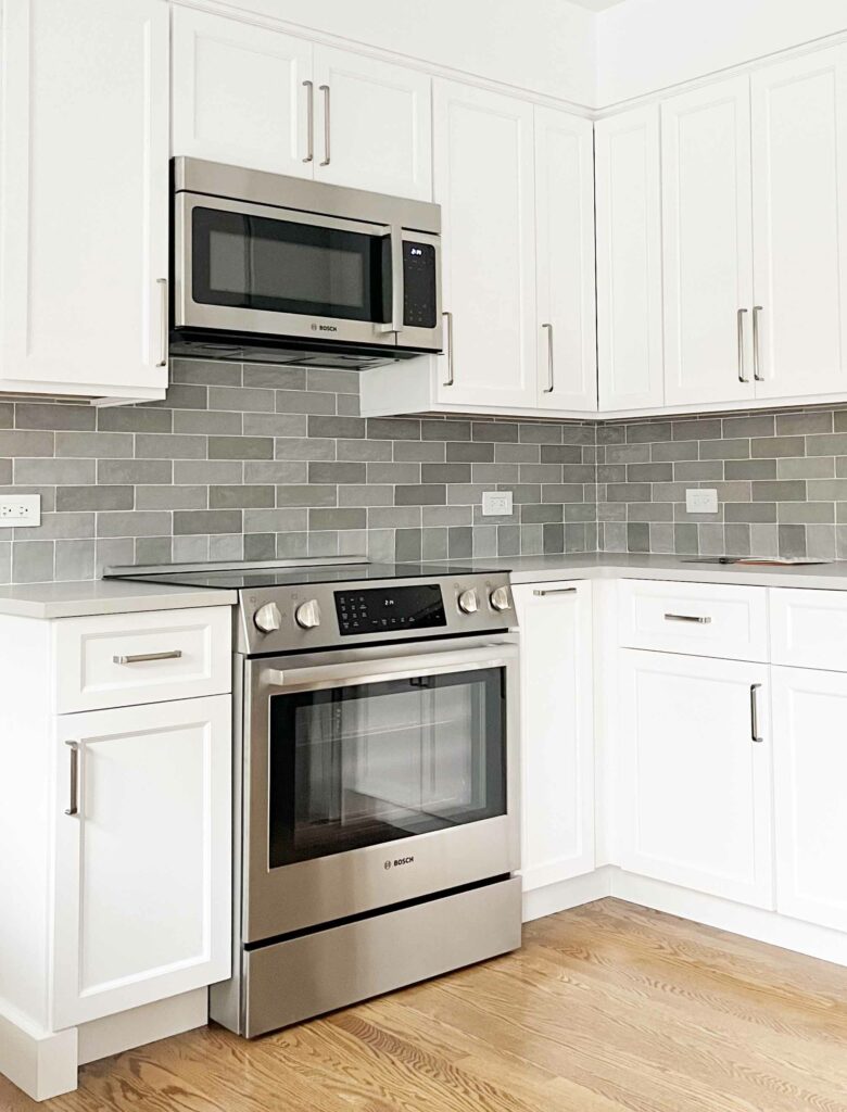 white cabinets with variegated gray blue tile backsplash and microhood