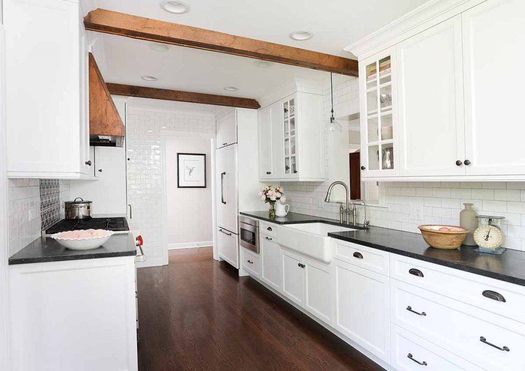 White Cabinetry with black countertops and wood beams on ceiling