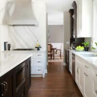 white painted kitchen with slab backsplash and metal hood pairs with dark stained island