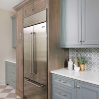 Stainless refrigerator with gray painted and stained wood cabinets and a checkerboard floor