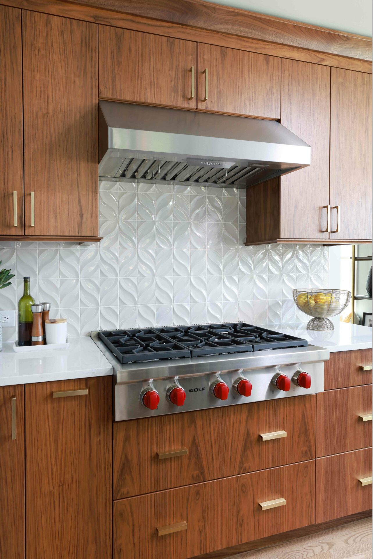 Walnut kitchen cabinets with textured tile, stainless steel hood and rangetop