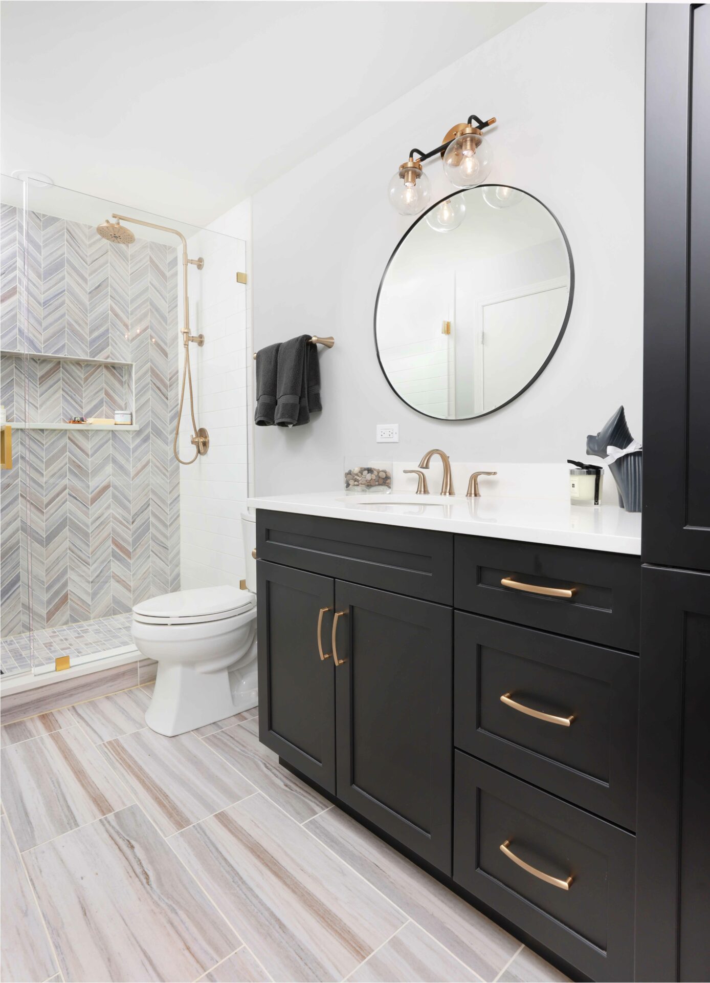 primary bathroom with chevron tile in shower, gold fixtures and dark vanity