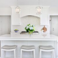 large white island with stools in white kitchen with decorative lighting