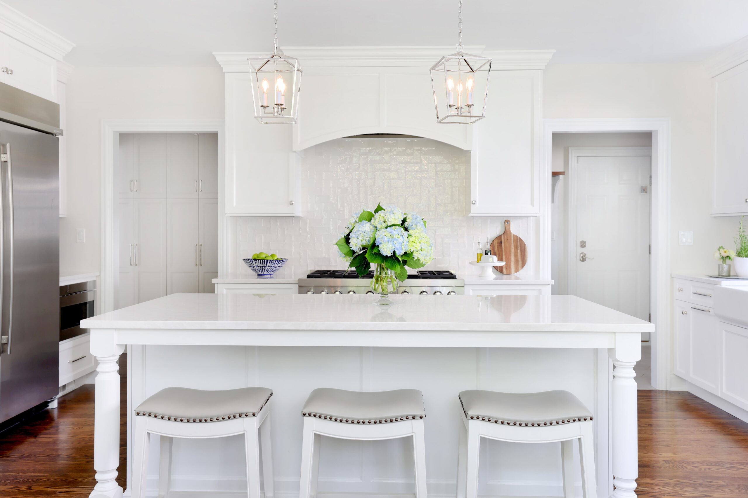 large white island with stools in white kitchen with decorative lighting