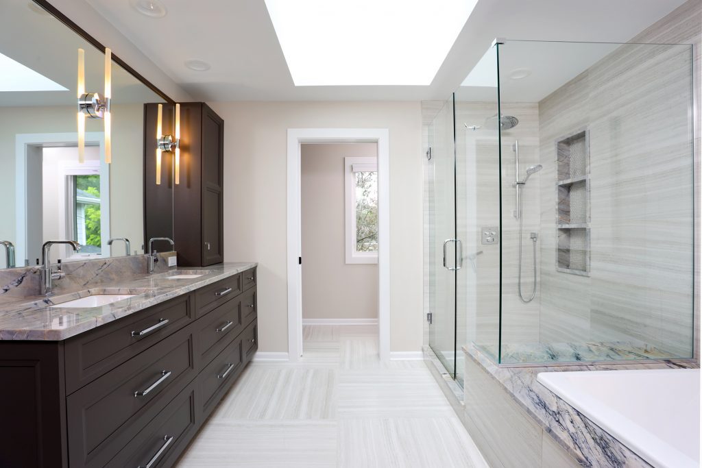 modern primary bathroom with separate shower and tub, skylight and dark double vanity