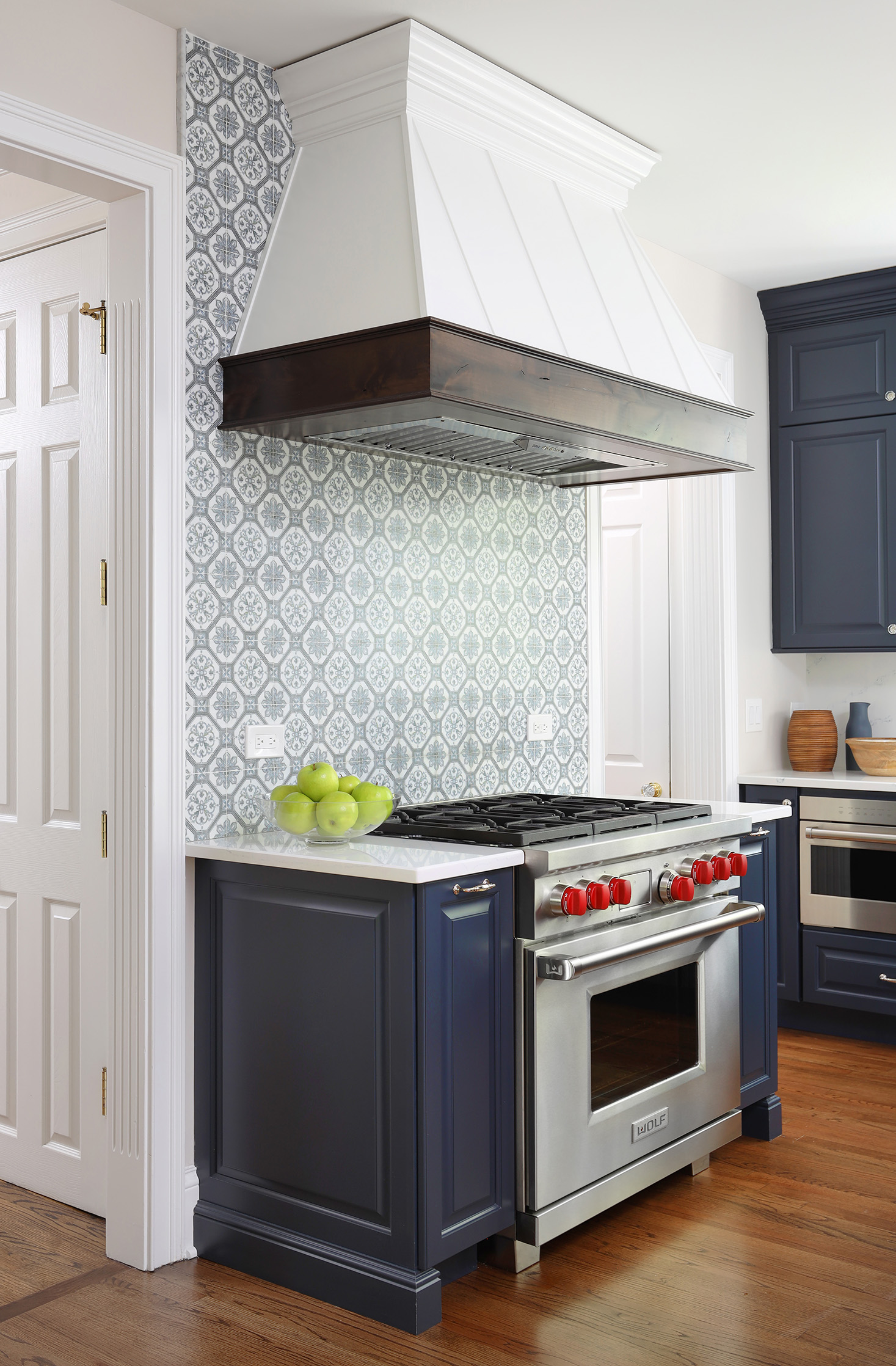 Blue kitchen cabinets with pattern backsplash tile and wood accent hood